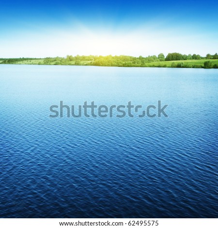 Blue sky with sun over water.