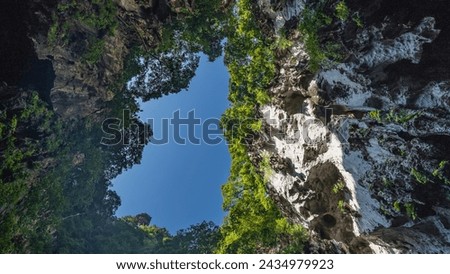 The blue sky surrounded by cliffs is visible from the cave. Green vegetation on steep rocky slopes. Bottom view. Malaysia. Batu caves. Kuala Lumpur