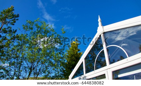 Blue sky, trees and clouds reflected in a garden conservatory.