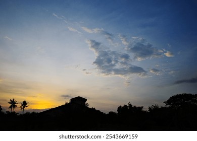 blue sky, white clouds, and trees and a barn silhouette at sunset. - Powered by Shutterstock