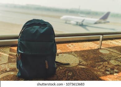 Blue small backpack standing on the floor at the airport on the background of flying and landing aircraft. Poisoned blue backpack on the floor. Forgotten Luggage. Lost hand Luggage.