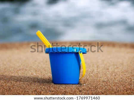 A blue small plastic bucket placed on sand with yellow stick on it
