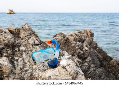 Blue Snorkle Or Diving Mask Located On The Rocks With Sea View On The Back.