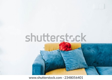 Blue sofa, 2 solid filled cushion, and a red cushion with a golden throw against white wall as background