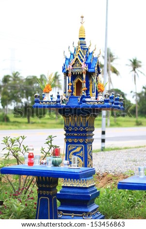 Blue spirit house in thailand with flowers in vases and some wreathes, joss house