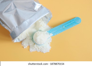 Blue Spoon With Infant Formula From The Package. Breastfeeding Replacement Concept. Nutrition Of The Child A Full Diet. Yellow Background