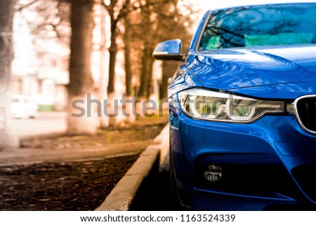 blue sports car with red tint and blurred trees in the background. Front grilles and headlights