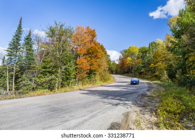 Blue Sports Car Traveling Down A Winding Road In Autumn Lined With Fall Colour - Ontario, Canada