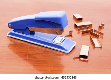 Blue stapler and piles of copper office staples on wooden office, closeup