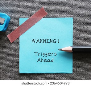 Blue stick note with handwritten text WARNING! triggers ahead - concept of knowing your triggers, to aware or identify emotion triggers when encountering something difficult