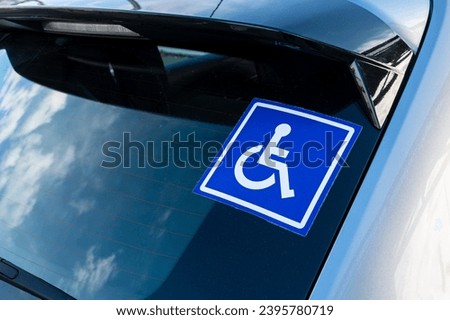 Blue sticker on the rear window of a car with a white pictogram representing a disabled person in a wheelchair. Concepts of transport and mobility of people with disabilities