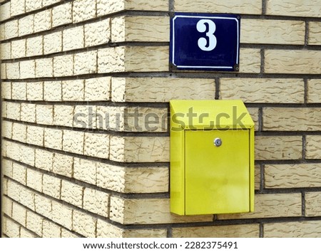 Blue street number 3 plate. Yellow home mail box and brick wall background. Pattern and texture. Minimalism. Around the corner. Stip, 2023 Macedonia