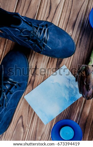 Blue suede shoes on a wooden brown background lie with blue candles in a candlestick and a brown artichoke. Fashionable women's blue boots. A pair of trendy warm boots.