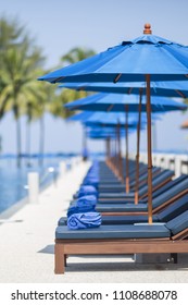 Blue Sun Umbrellas And Deck Chairs By A Swimming Pool