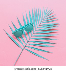 Blue Sunglasses Are On The Branch Of A Palm Tree On A Pink Background. Fashion Flat Lay.