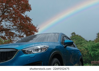 Blue SUV car covered with raindrops against green forest and rainbow sky. Car parked at outdoor parking lot. Road trip travel. Adventure travel in national park. Safety driving in rainy season concept - Powered by Shutterstock