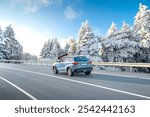 Blue suv car driving on nature road in snowy forest in winter. Snowy winter road landscape in nature trip. Winter travel in mountain road scenery. Winter landscape on the highway in snowy mountains.