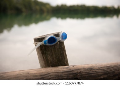 Blue Swimming Googles On A Wooden Pole With Large Lake In Background