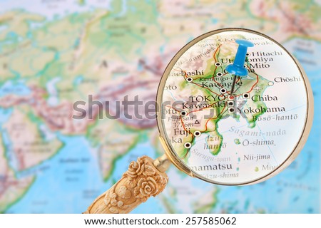 Blue tack on map of the world with magnifying glass looking in on Tokyo, Japan
