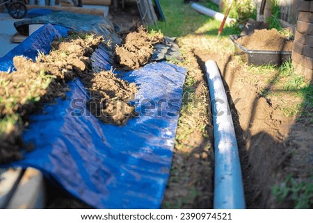 Blue tarp, black mixing tub container with dirt, underground PVC pipe buried in trench installation, rainwater drainage system connected gutter of residential house, Dallas, Texas, USA. Piping sewer