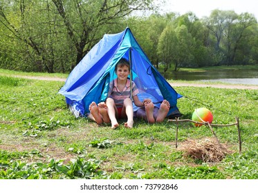From blue tents on a grassy glade meadow legs stick out and a little boy sitting in it and smile