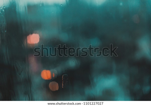 Blue texture of drops on the glass, blurred city\
lights in the evening\
city.