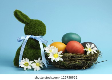 Blue theme Happy Easter scene still life with grass bunny rabbit with rainbow color eggs in a nest with white daisies.