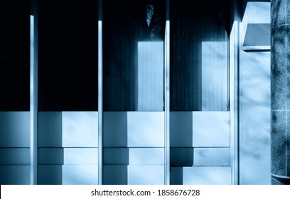 Blue Tinted Image Of Facade Of 1980s Office Building With Graded High Contrast Shadowing Cast Over The Windows On Sunny Day. Office Blinds Visible Through Two Of Four Windows