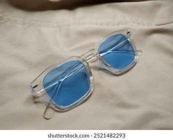 blue tinted sunglasses with transparent frames on a beige cloth backdrop