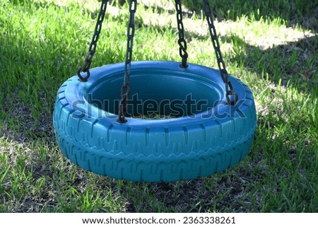 A blue tire swing hanging from 4 chains with a plastic tire instead of rubber. This is a closeup shot of the swing with green grass in the background.