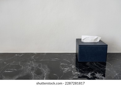 Blue tissue box with white paper tissues on black marble table with copy space for text.
