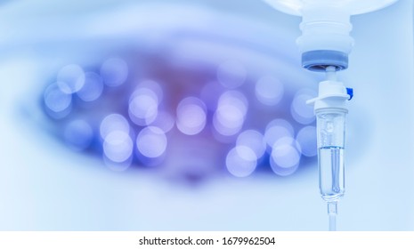 Blue tone picture of syringe pump with blurred background.Intravenous fluid used in the operating room while doctor perform surgery. Surgical lamp in background with red highlight. Medical concept.