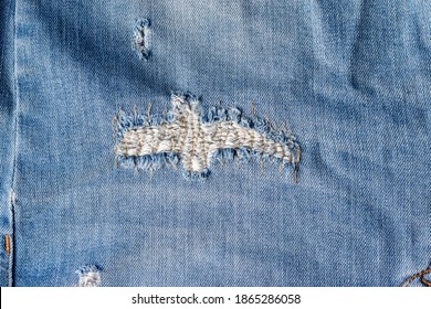 Blue Torn Jeans Fabric Texture. Distressed Denim With Sewn-up Hole And Seam Background