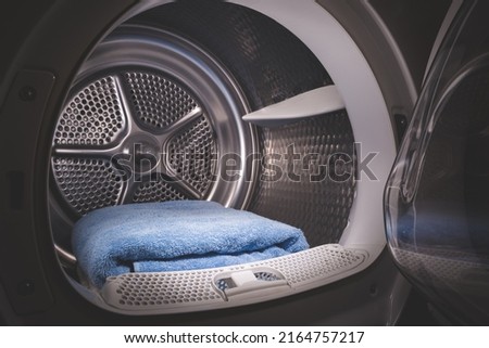 Blue towels are stacked in the tumble dryer. Laundry. Clean concept. Washing machine with open door. Toned