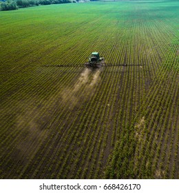 A blue tractor moves through the spring field and sprays fertilizers on plants planted on it. Spring processing of agricultural crops. View from above. Aerial view - Shutterstock ID 668426170