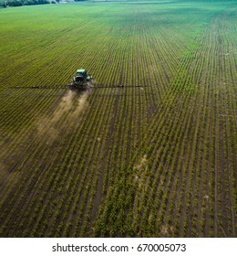 A blue tractor moves through the spring field and sprays fertilizers on plants planted on it. Spring processing of agricultural crops. View from above. Aerial view - Shutterstock ID 670005073