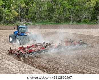 Blue tractor pulling a red field cultivator to prep the field for spring planting.
