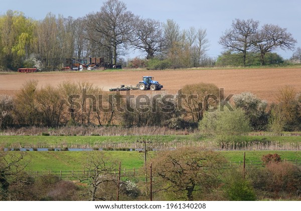 A blue tractor smoothing the ground in a farm with
trees and grass around