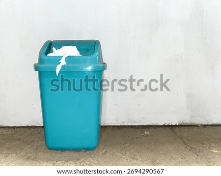 Blue trash bin filled with garbage against a clean white background, symbolizing waste management and environmental awareness.