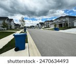 Blue trash cans, including a yellow recycle bin, beside the street on trash day in an Indiana Neighborhood with copy space.