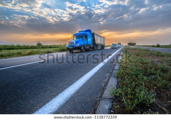Blue truck on highway at\
sunset. 