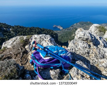 Blue Turist Backpack And Walking Sticks On The Edge Of The Cliff With The Sea View. Mallorca. Tramuntana. Camino De Archiduque.