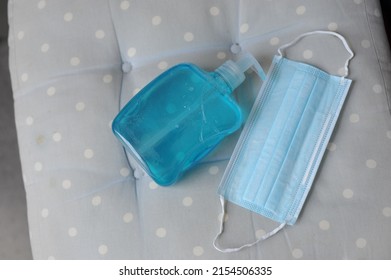 Blue Turquoise Hand Sanitizer Gel And Disposable Face Mask For Infection Control. Close Up Of Medical Items For Coronavirus Protection On Blue Spotty Cushion. 