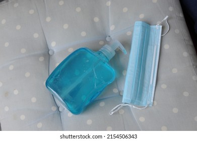 Blue turquoise hand sanitizer gel and disposable face mask for infection control. Close up of medical items for coronavirus protection on blue spotty cushion. 