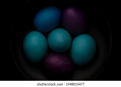 Blue, Turquoise, And Purple Easter Eggs In A Bowl With Strong Shadows And Dark Background.