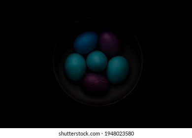 Blue, Turquoise, And Purple Easter Eggs In A Bowl With Strong Shadows And Dark Background.