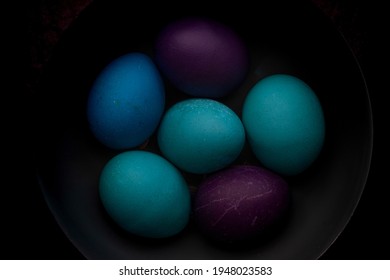 Blue, Turquoise, And Purple Easter Eggs In A Bowl With Strong Shadows And Dark Background.