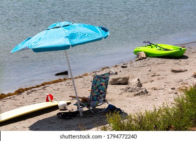 A Blue Umbrella Stuck In The Sand With A Green Kayak On A Beach