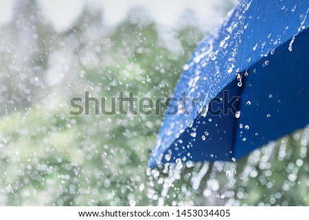 Blue umbrella under heavy rain against nature background. Rainy weather concept.