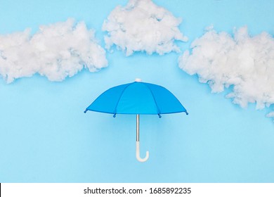 Blue Umbrella Underneath Puffy Coat And Clouds On A Light Blue Background￼